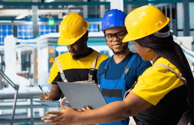 Three technicians in hard hats reviewing job documentation together on a plant floor